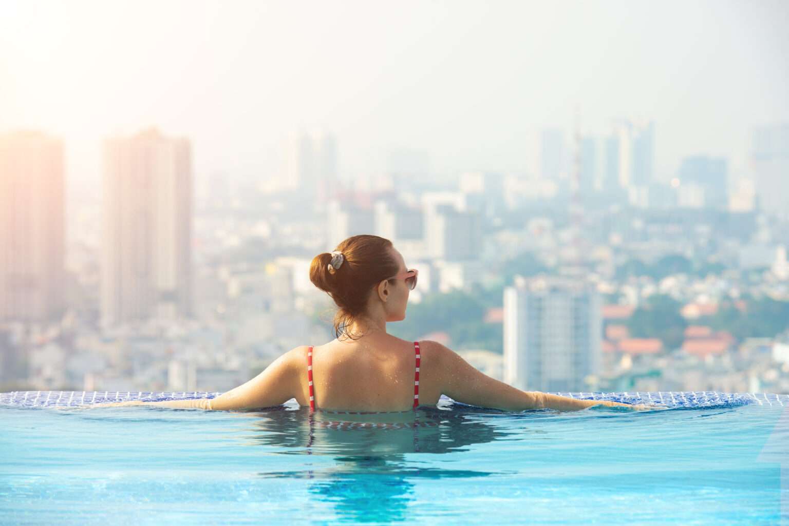 Happy woman enjoying in the rooftop pool of the hotel on the background of big Ho Chi Minh City, Vietnam